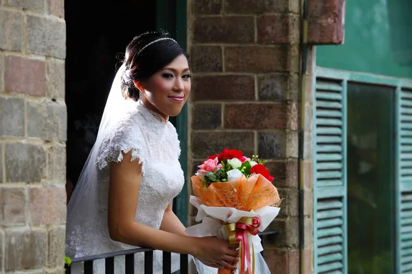 Beautiful bride with bunch of flowers standing on terrace — Stock Photo, Image