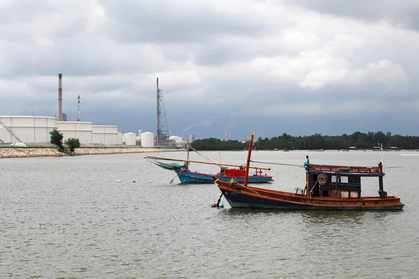 Wooden fishing boat near crude oil tank terminal — Stock Photo, Image