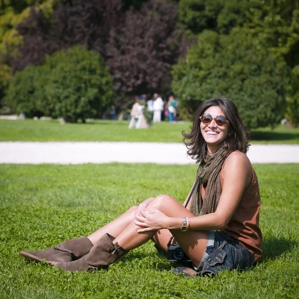 Красивая улыбающаяся девушка в шарфе и солнцезащитных очках на газоне — стоковое фото