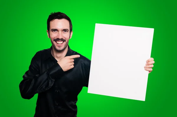 Uomo sorridente in possesso di bordo bianco vuoto sul backgroud verde — Foto Stock