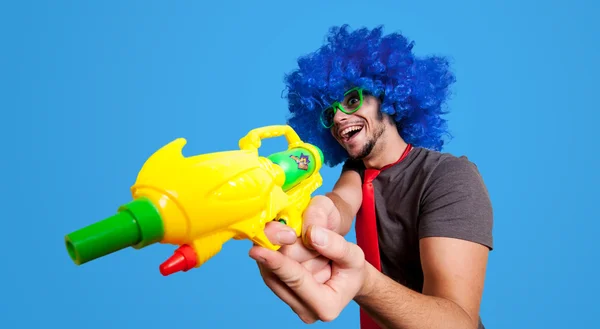 Cara engraçado com peruca azul e pistola de água — Fotografia de Stock