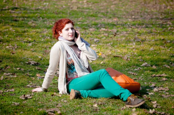 Chica de pelo largo rojo en el parque en el teléfono —  Fotos de Stock