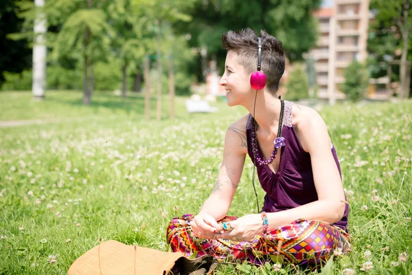 Schöne Hipster-Frau mit kurzen Haaren, die im Park Musik hört — Stockfoto