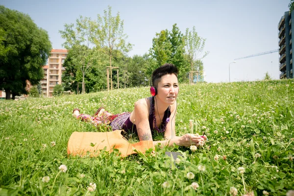 Schöne Hipster-Frau mit kurzen Haaren, die im Park Musik hört — Stockfoto