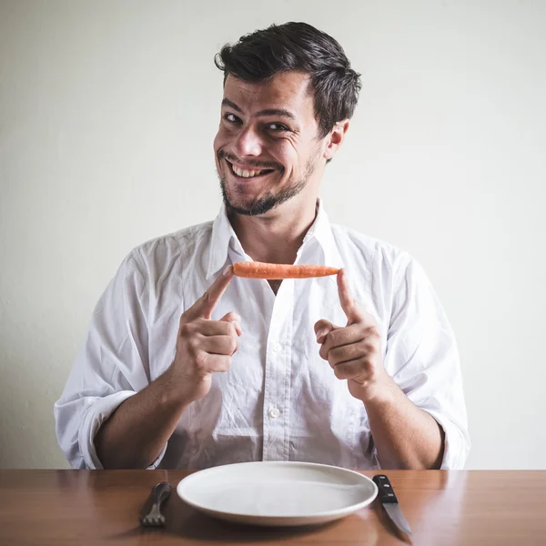 Giovane uomo elegante con camicia bianca mangiare carota — Foto Stock