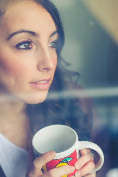 Mooie vrouw met cup geconfronteerd met via venster — Stockfoto