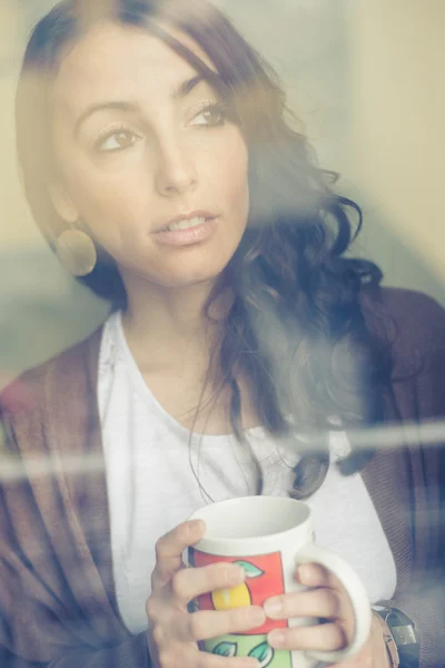 Vacker kvinna med kopp inför genom fönster — Stockfoto