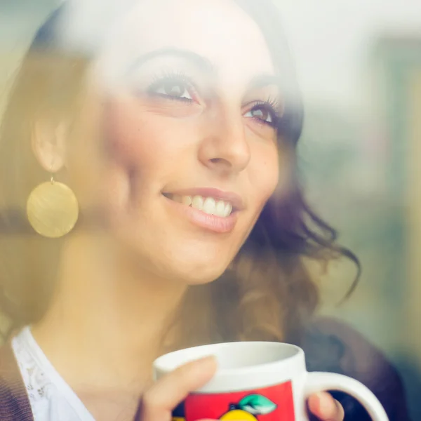 Mooie vrouw met cup geconfronteerd met via venster — Stockfoto