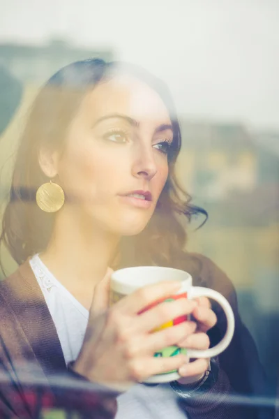 Mooie vrouw met cup geconfronteerd met via venster — Stockfoto