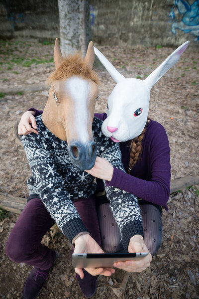 Young hipster cuople horse and rabbit mask using tablet