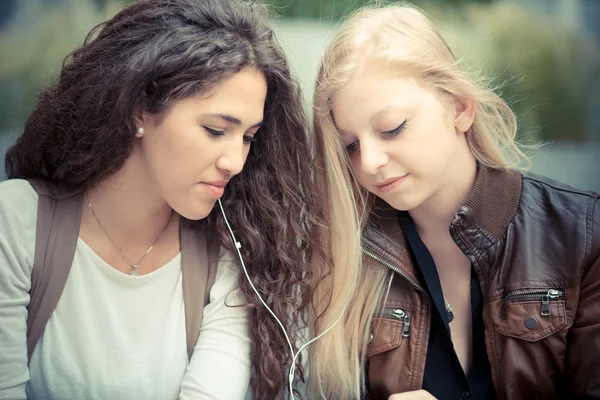 Rubia y morena hermosas mujeres jóvenes con estilo utilizando inteligente — Foto de Stock