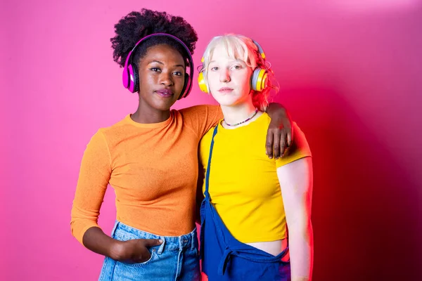 Två Multietniska Unga Kvinnor Kramas Lyssna Musik Ler Isolerad Rosa — Stockfoto