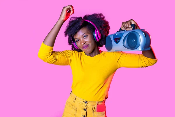 若いです黒の女性リスニング音楽ダンス保持ヴィンテージBoomboxと身に着けています無線ヘッドフォン隔離されたピンクの背景 — ストック写真