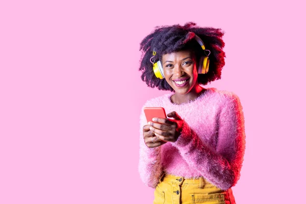 ワイヤレスヘッドフォンを着用したスマートフォンサーフィンウェブを使用して若い黒人女性隔離された背景 — ストック写真