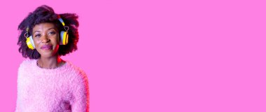 Genç siyahi kadın münferit müzik pozu veriyor kablosuz kulaklıklar arkadaş canlısı ve rahat pembe reklam alanı arka planında pozitif gülümsüyor