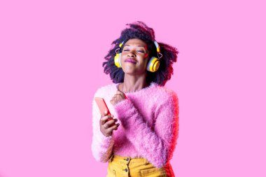 Genç siyahi kadın dans ediyor. Akıllı telefon kablosuz kulaklıkla müzik dinliyor. Gülümsüyor. 