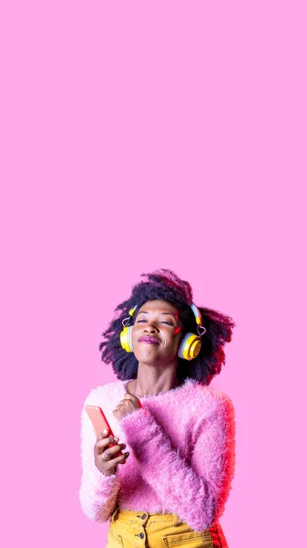 若い黒人女性がスマートフォンのワイヤレスヘッドフォンを使用して音楽を聴いて踊る笑顔幸せな気持ちフリー孤立した広告コピースペースの背景 — ストック写真