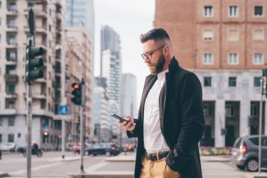 Kafkasyalı genç iş adamı akıllı telefon kullanarak dışarıda yürüyor. İnternet üzerinden 5G teknolojisi kullanıyor, video yayını izliyor ya da oyun oynuyor.
