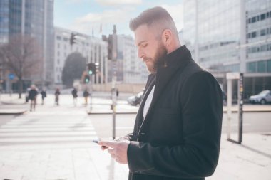 Genç, zarif, başarılı, beyaz, açık havada akıllı telefon taraması yapan internet uzaktan kumandası kullanarak e-postaları kontrol eden bir adam.