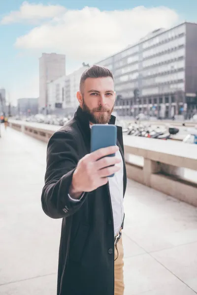 若いですひげを生やした白人エレガントな男屋外で使用してスマートフォンビデオ通話または自己撮影 — ストック写真
