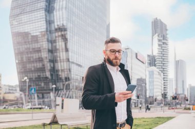Genç, beyaz, çağdaş iş adamı uzaktan kumandayla akıllı telefon kontrolü yapıyor.