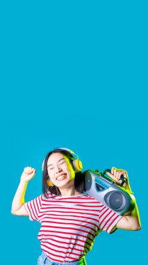 Genç Asyalı kadın dans ediyor müzik kasedi dinliyor. Elinde müzik kaseti var. Kablosuz kulaklık takıyor özgürce gülümsüyor.