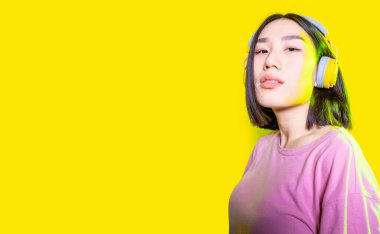 Evde kablosuz kulaklık takan Asyalı bir kadın kameraya bakıyor kendine güveniyor ve müzik dinlerken pozitif kadın gücünün tadını çıkarıyor. Kesilmiş afiş.