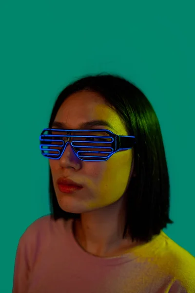 戴耳机和带着绿色背景眼镜的未来变相科幻眼镜的年轻女性 — 图库照片