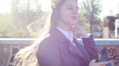 Genç beyaz kadın açık havada müzik dinliyor kulaklık takıyor akıllı telefon sörfü ağı kullanıyor.