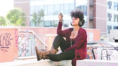 Genç siyahi kadın dans ediyor, müzik dinliyor, kulaklık takıyor, akıllı telefon eğleniyor.