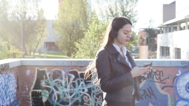 若い白人女性スマートフォンサーフィンのウェブを使用してイヤフォンを身に着けている音楽を聞く屋外 — ストック動画