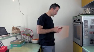 Evde fırında akıllı telefon kullanan yetişkin bir adam. Teknoloji, internette arama, ev yapımı kibir.