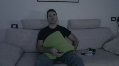 Evde oturan yetişkin bir adam, uzaktan kumandayla TV seyrediyor. Eğlence, canlı uygulama, cümbüş konsepti.