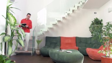 Evde evde tek bir yetişkin adam tablet bilgisayar kullanarak yerde oturuyor. Uzaktan kumandalı, küçük işletmeli, akıllı çalışma konsepti.