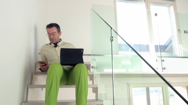 自宅の階段にスマートフォンやタブレットを使用して座っているシングル大人の男性屋内 リモートワーク 中小企業 スマートワーキングコンセプト — ストック動画