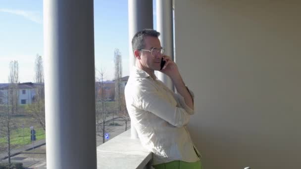自宅のテラスで大人の男性柔軟な労働者が会話を持つスマートフォンを話してリモート作業 ビジネスコンセプト — ストック動画
