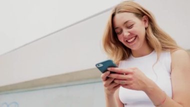 Yavaş çekim genç bayan dışarıda akıllı telefon taraması kullanarak şifreli para ticareti yaparak gülüyor.