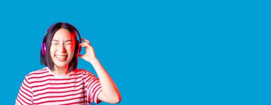 Huzurlu Asyalı kadın mavi arka planda izole edilmiş. Kablosuz kulaklıklar dinliyor. Gülümsüyor.