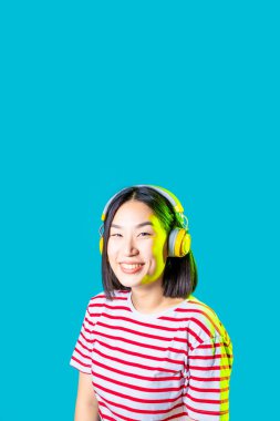 Sakin Asyalı kadın mavi arka planda izole edilmiş. Kablosuz kulaklıklar dinliyor. Gülümsüyor.