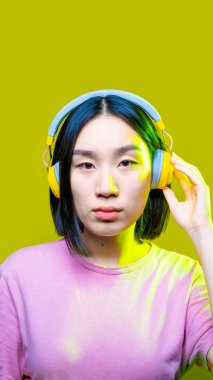 Genç Asyalı kadın arka planı izole ederek müzik kulaklıklarını ciddi şekilde dinledi - dikey afiş