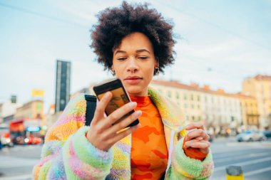 Açık havada akıllı telefon mesajları kullanan ya da canlı yayın yapan video izleyen genç bir ırk kadını.