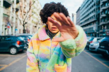 Genç, kıvırcık saçlı, açık havada el hareketleriyle dans eden kadın.