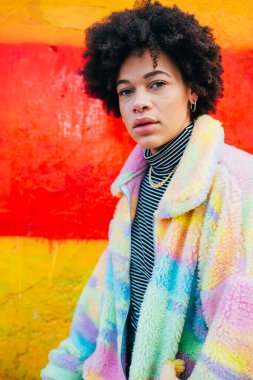 Genç, melez, kıvırcık saçlı, dışarıda poz veren, şık görünümlü, kendine güvenen bir kamera.