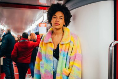 Genç melez kadın yer altında seyahat ediyor düşünceli bir şekilde kameraya sakin ve kendinden emin bakıyor.