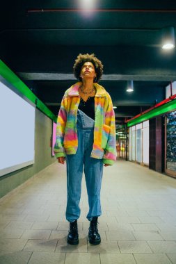 Dalgın melez kıvırcık saçlı, stil sahibi kadın. Kapalı metrolarda poz verip hayalperest kadınlara bakıyor.