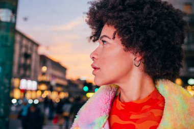 Şehrin dışında poz veren, ciddi ve kendinden emin genç melez bir kadın portresi