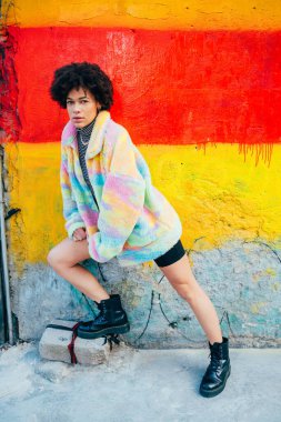 Tarz sahibi genç siyah kadın, kıvırcık saçlı, dışarıda poz veren ciddi ve havalı, kendine güvenen bir kadın.