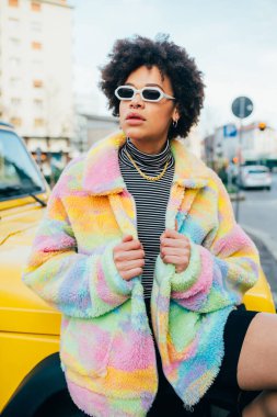 Güneş gözlüğü takan şık afro genç bir kadın. Dışarıda poz veriyor. Havalı, havalı bir tavır takınıyor.