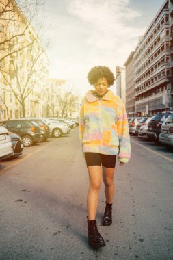 Sade, siyah, kıvırcık saçlı, şık, havalı bir kadın. Şehir dışında yürüyor.