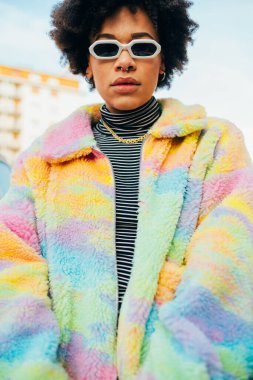 Genç siyah stil kıvırcık saçlı kadın dışarıda poz veriyor güneş gözlüğü takıyor.